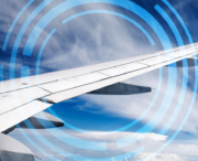View of an airplane wing in flight against a blue sky with clouds, overlaid with blue circular digital graphic elements.