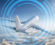 A commercial airplane flies above the clouds, surrounded by blue digital circular graphics suggesting technology or connectivity in aviation.