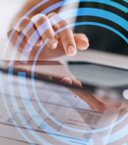 A person uses a tablet on top of printed financial documents, with blue digital circular graphics overlaid on the image.