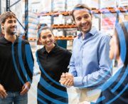 Four people stand and converse in a warehouse, surrounded by shelves with boxes. Blue concentric circles are digitally overlaid on the image.