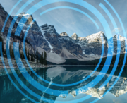 Snow-capped mountains reflected in a calm lake, overlaid with translucent blue concentric circles and lines.