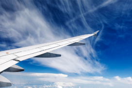 View of an aeroplane wing in flight against a blue sky with wispy white clouds.