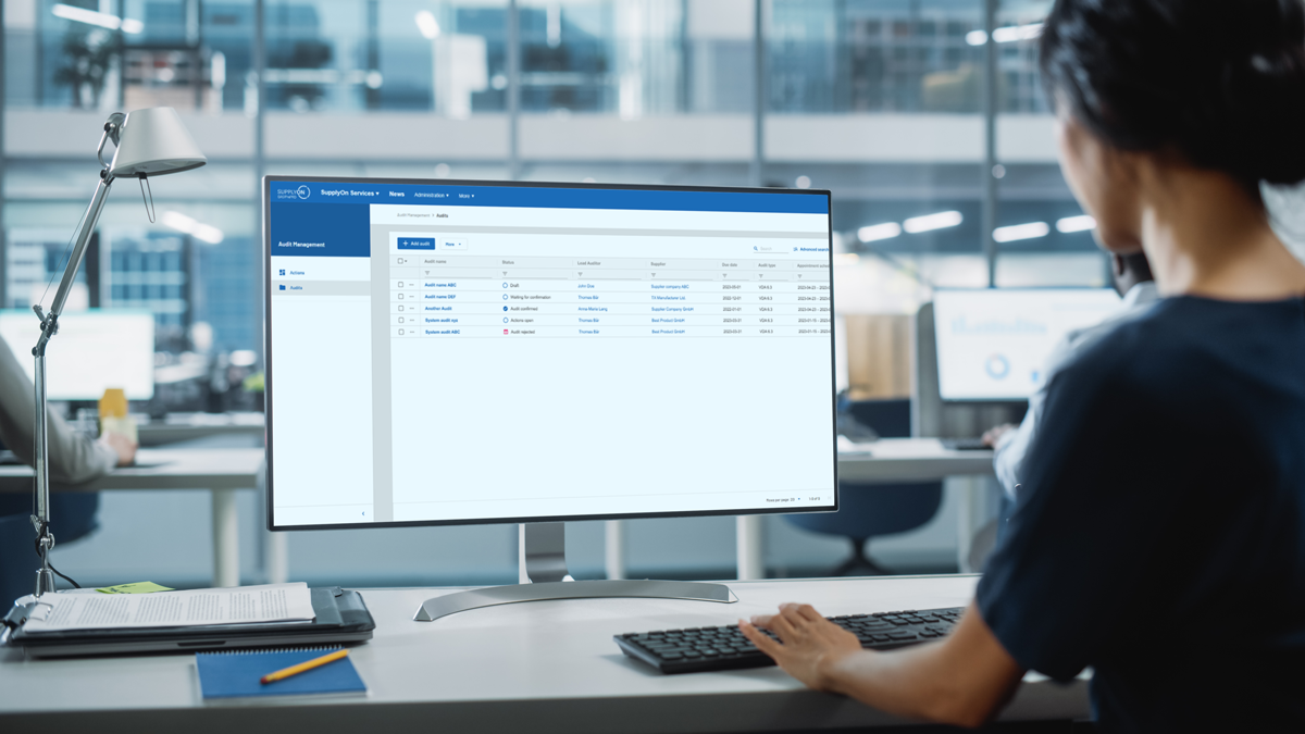 Person working at a desk in a modern office, viewing a staff management software interface on a large computer monitor.