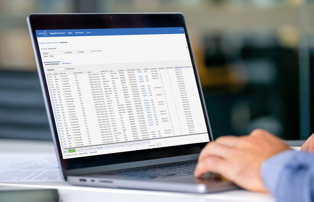 A person uses a laptop displaying a supply chain management software interface with a table of shipment details and tracking statuses.
