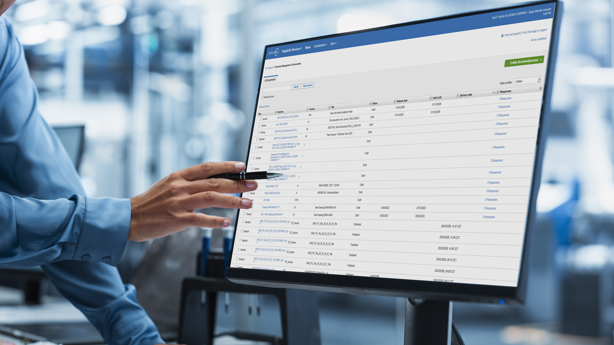 Person pointing at a computer monitor displaying a data management software interface with multiple rows and columns of information visible.