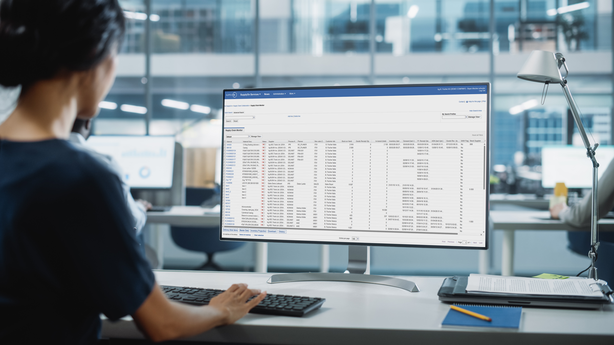 Person working at a desk, viewing a large spreadsheet or database on a desktop computer monitor in a modern office setting.