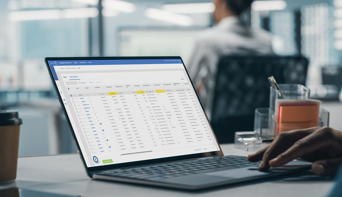 A person works on a laptop displaying a data management dashboard with tables and filters in an office setting.